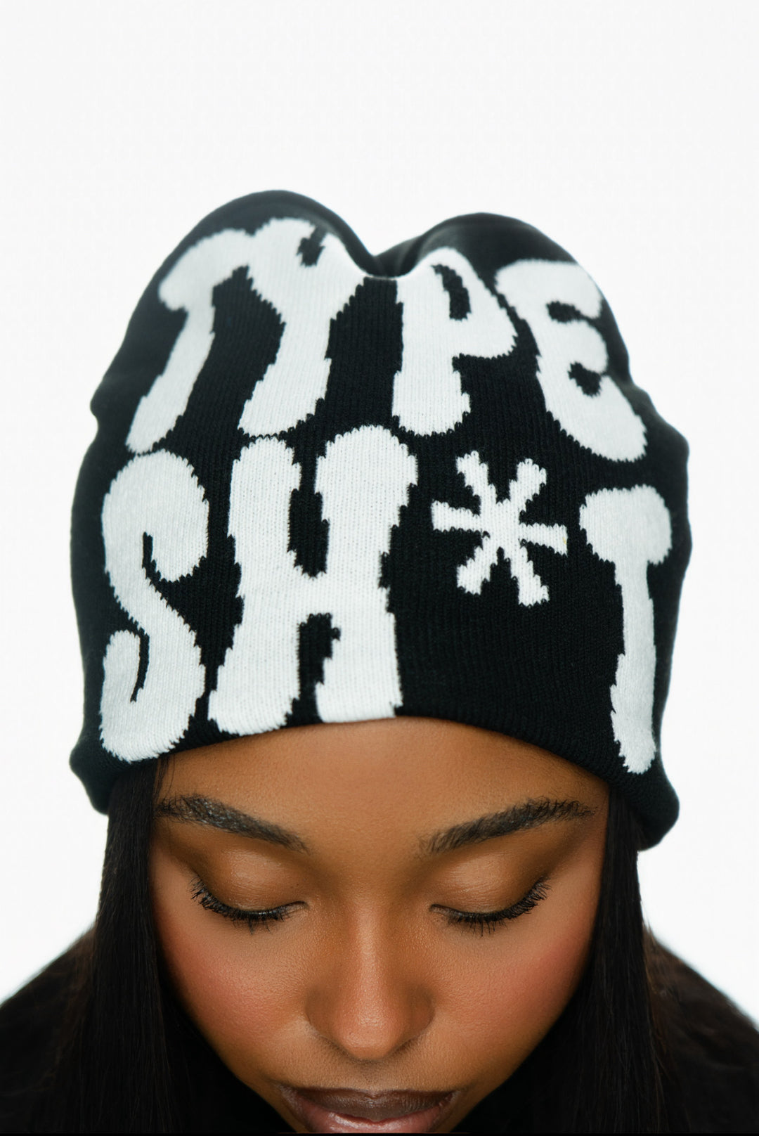 Black beanie with bold white text, worn by a person looking down, showing part of their face.