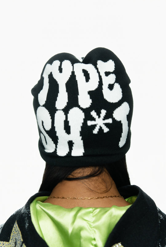 Black beanie with bold white text reading "TYPE SH*T," worn over a green satin shirt.