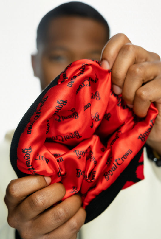 A hand holding a red satin cap lined with "Royal Crown" printed in black.