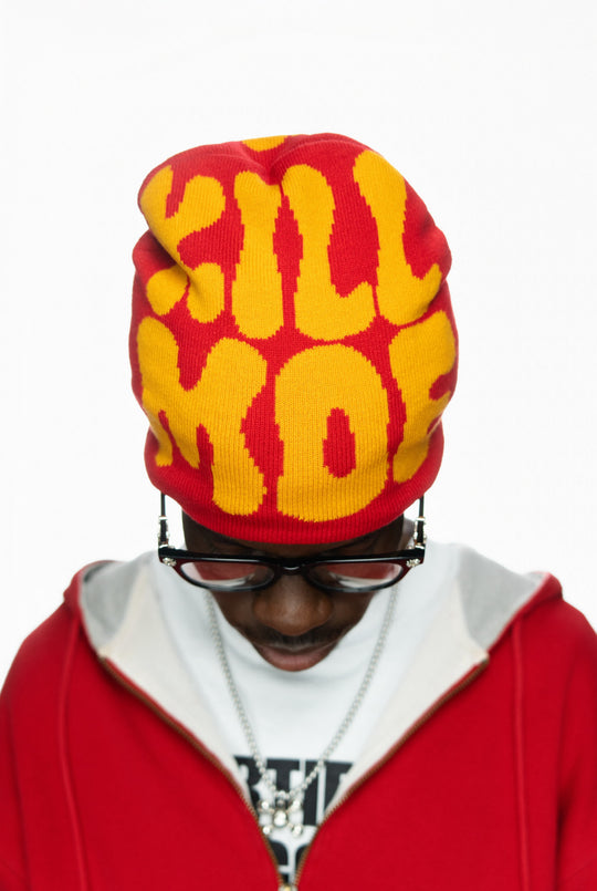 Person wearing a red and yellow beanie with bold text, looking down, in a red jacket.