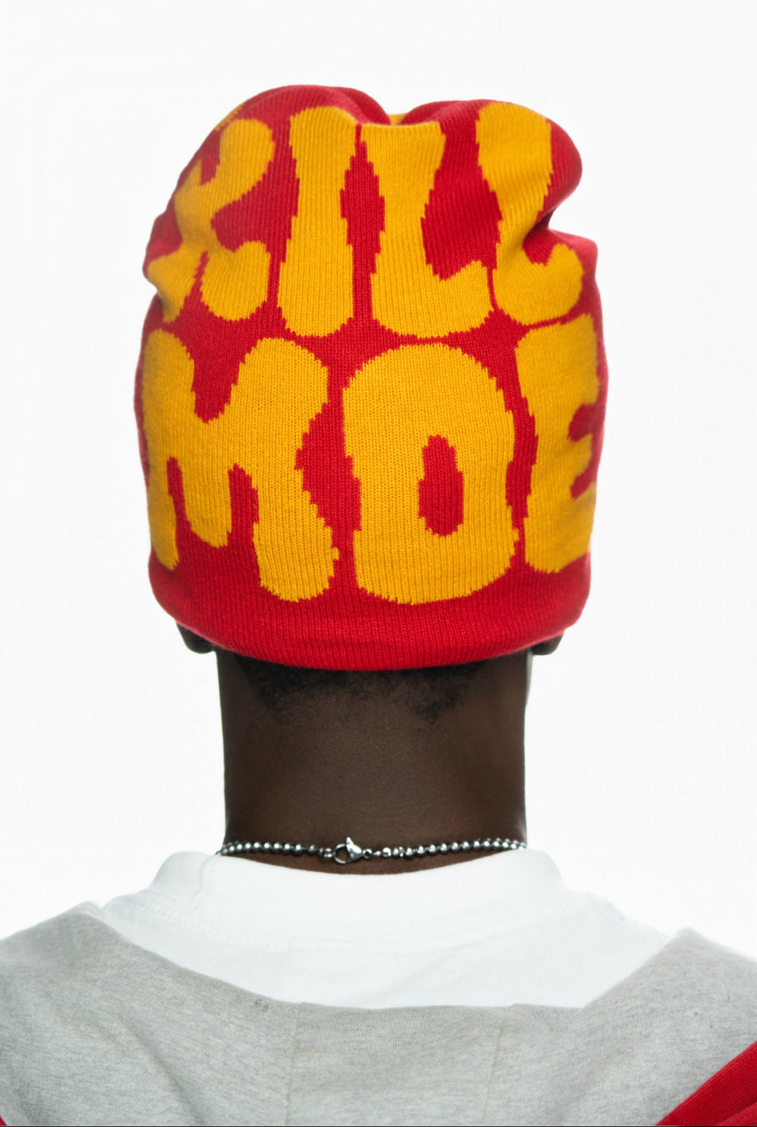 Red and yellow beanie with bold lettering worn by a person, viewed from the back.