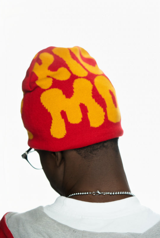Red and yellow beanie with bold letters worn by a person viewed from the back.