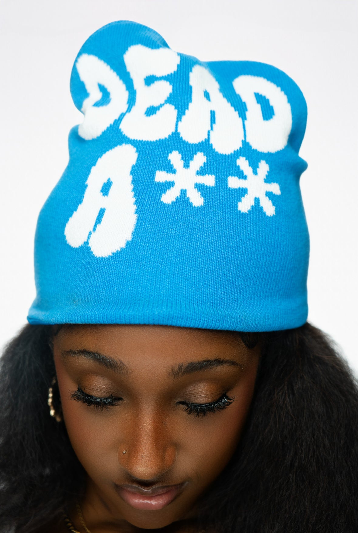 Person with dark hair wearing a blue beanie featuring bold white text and designs.