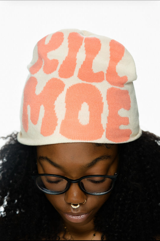 A person wearing a cream hat with pink text, glasses, and multiple nose piercings.