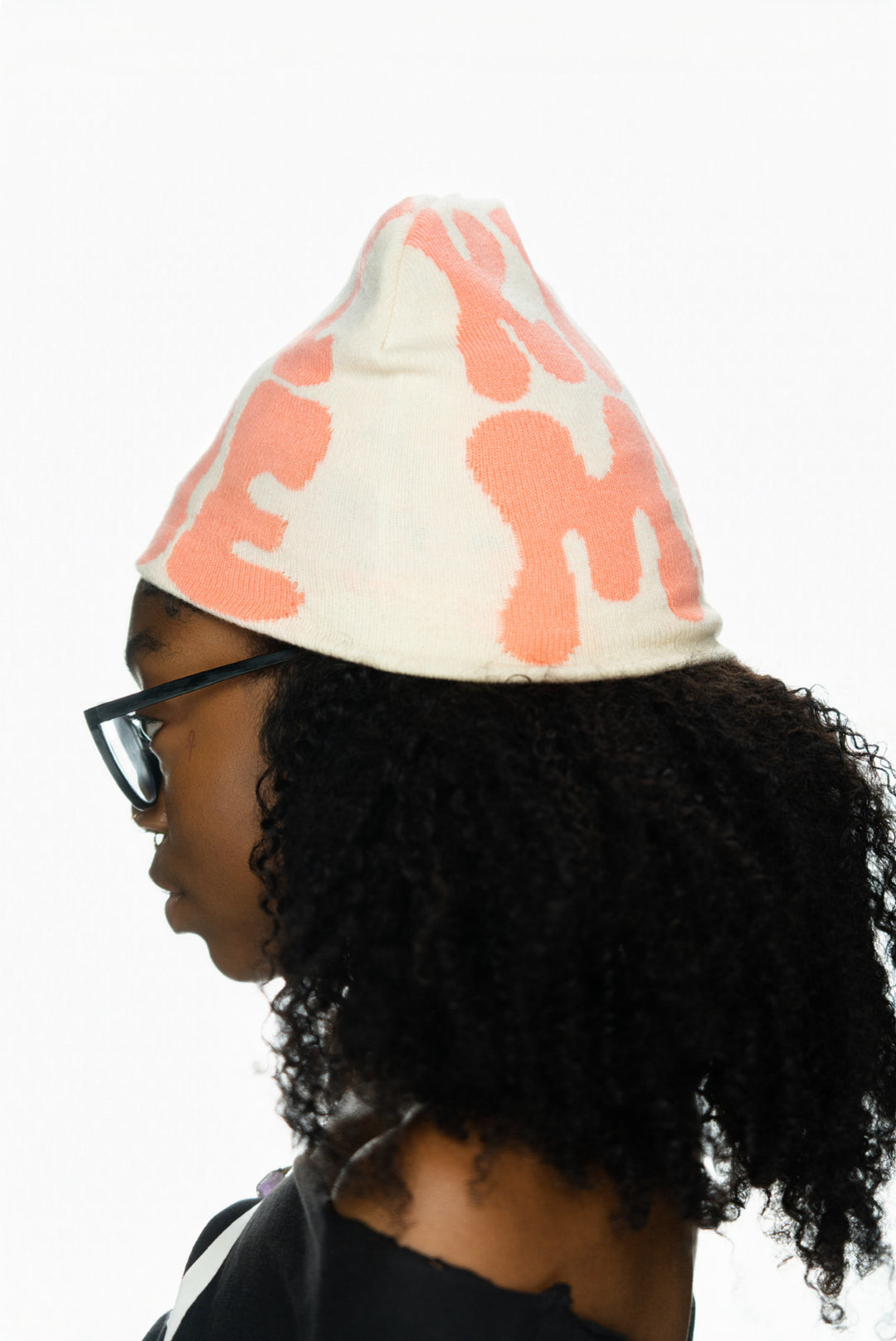 Person with curly hair wearing a light-colored hat featuring bold pink patterns.