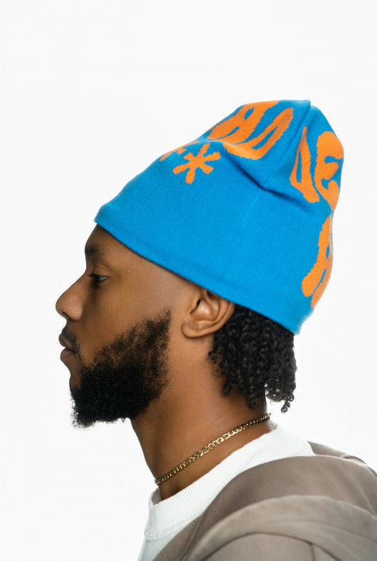 Blue knitted beanie with orange lettering modeled by a man with a short beard and gold chain.