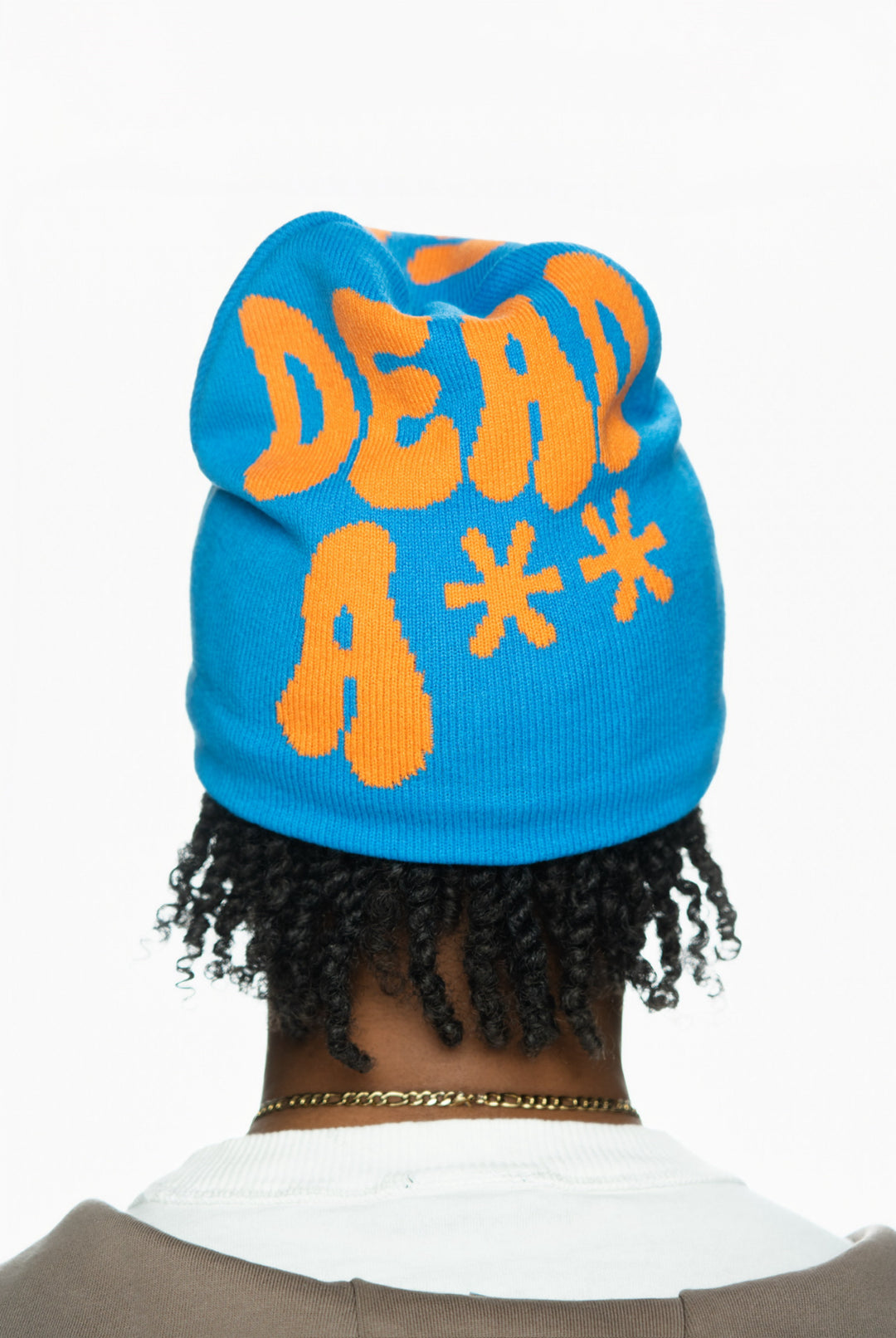 Blue beanie with bold orange text reading "DEAD A**" worn by a person with curly hair.