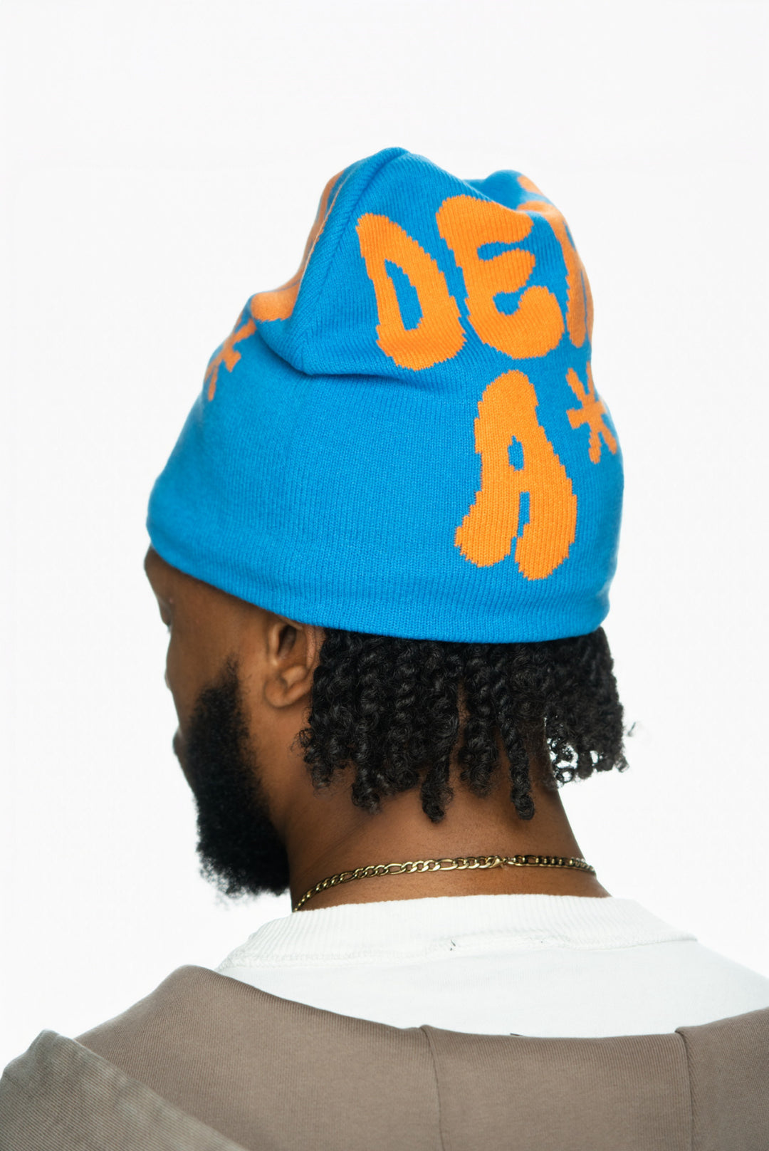 Blue beanie with orange text, worn by a person with short, curly hair and gold chain.