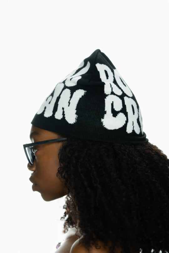 Child with curly hair wearing a black beanie featuring bold white text, viewed from the side.