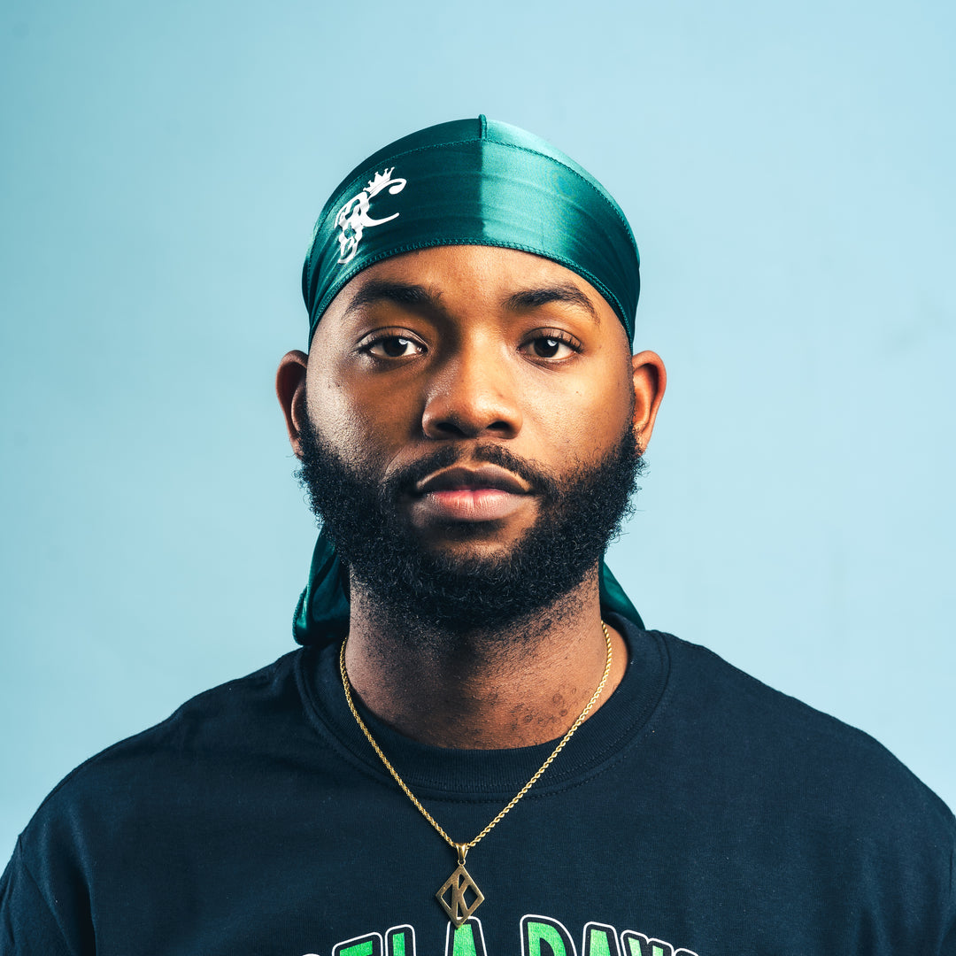 A man wearing a green silk durag with a logo on the forefront.